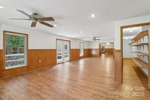 119 Legacy Ln, Harmony, NC 28634 - unfurnished living room featuring a wainscoted wall, ceiling fan, light wood-style flooring, wood walls, and a textured ceiling