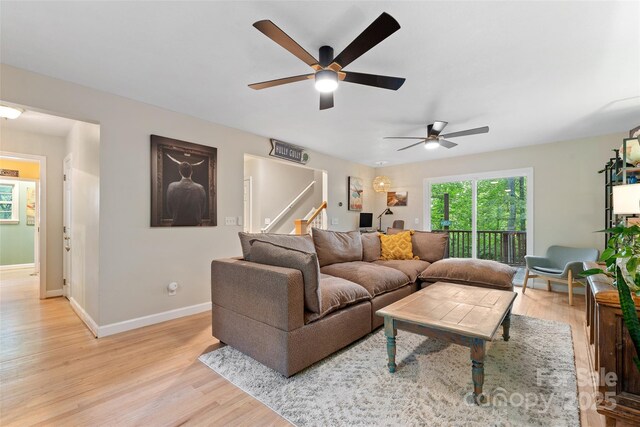 living room featuring stairway, baseboards, a ceiling fan, and light wood finished floors