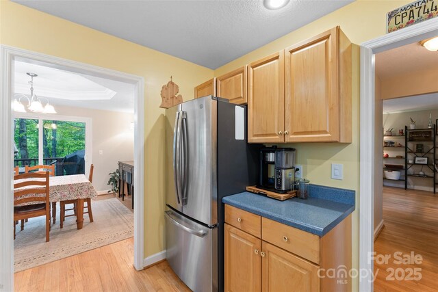 kitchen featuring light wood-style floors, freestanding refrigerator, a notable chandelier, and dark countertops