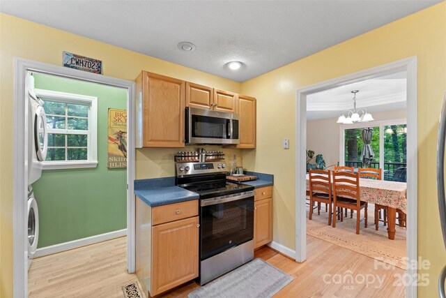 kitchen with light wood-type flooring, stacked washer and dryer, dark countertops, and stainless steel appliances
