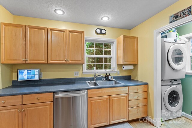 kitchen featuring dark countertops, dishwasher, a textured ceiling, a sink, and stacked washer / drying machine