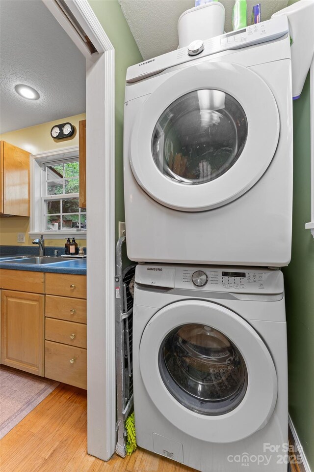 clothes washing area with stacked washer and dryer, laundry area, a sink, light wood finished floors, and a textured ceiling