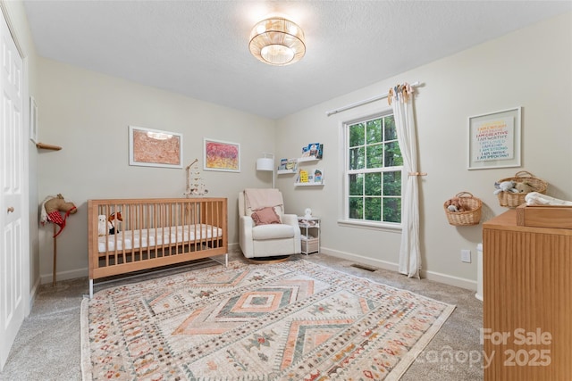 bedroom with a textured ceiling, visible vents, a crib, baseboards, and carpet flooring