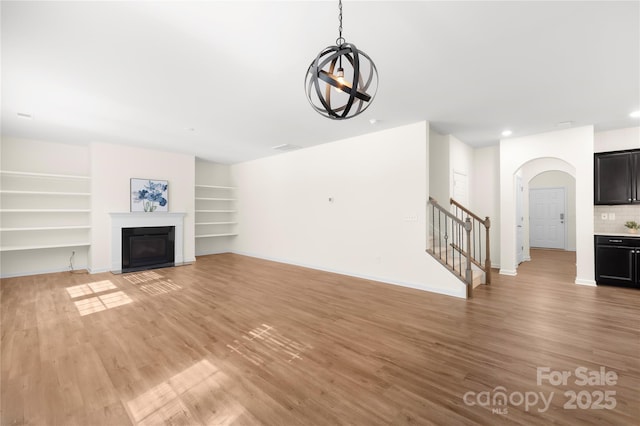 17413 Caddy Ct, Charlotte, NC 28278 - unfurnished living room featuring arched walkways, stairway, light wood-type flooring, a glass covered fireplace, and built in features