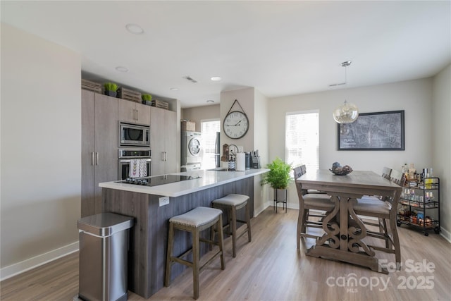 kitchen with stainless steel appliances, a peninsula, baseboards, a kitchen bar, and washer / clothes dryer