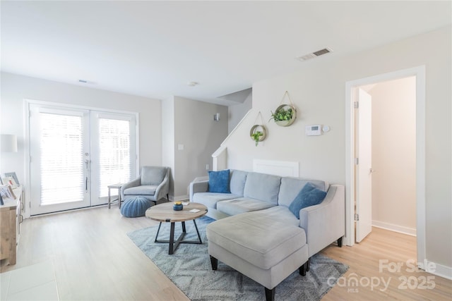 living room with light wood-style floors, baseboards, visible vents, and stairs