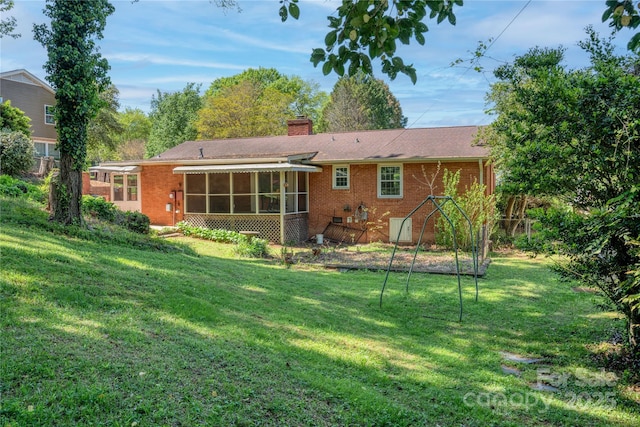 back of house featuring a sunroom, a chimney, brick siding, and a lawn