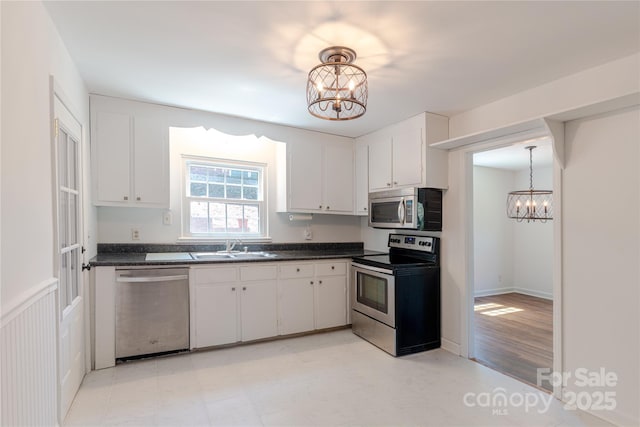 kitchen with appliances with stainless steel finishes, a sink, a notable chandelier, and dark countertops