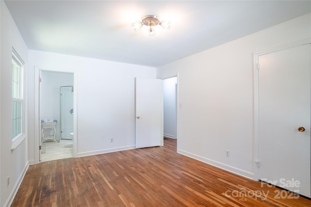 unfurnished bedroom featuring wood finished floors, baseboards, and connected bathroom