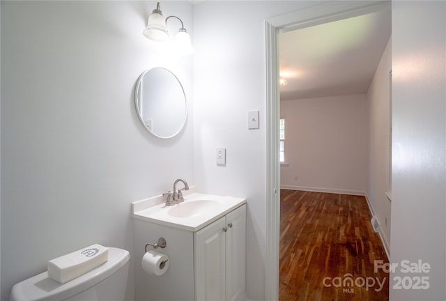 half bathroom featuring toilet, wood finished floors, and vanity