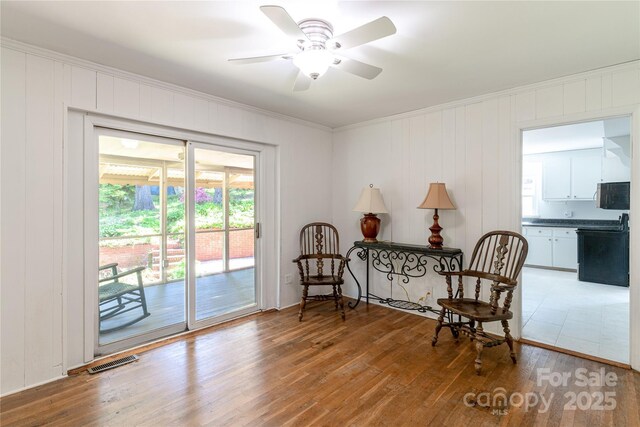 sitting room with crown molding, visible vents, a ceiling fan, and wood finished floors