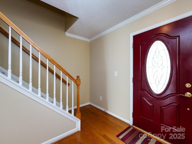 entrance foyer featuring a textured ceiling, baseboards, wood finished floors, stairway, and ornamental molding