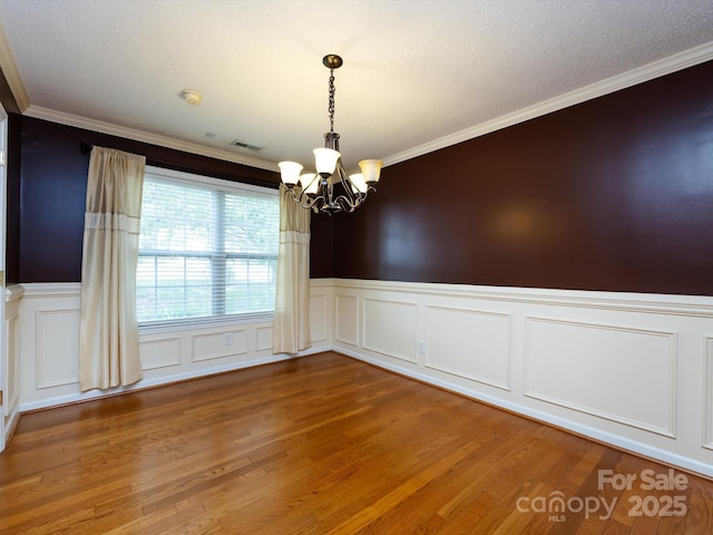 empty room with visible vents, crown molding, wainscoting, a chandelier, and light wood-style flooring