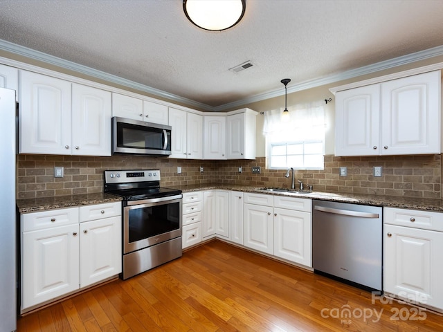kitchen featuring stainless steel appliances, light wood-style flooring, a sink, dark stone countertops, and visible vents