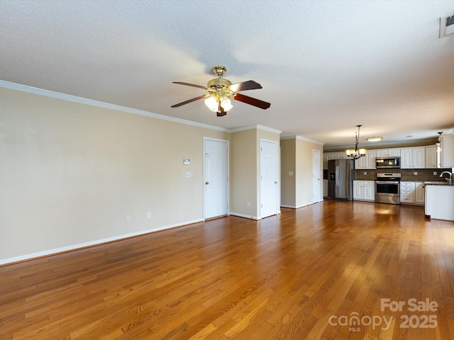unfurnished living room with dark wood-style floors, ornamental molding, a sink, baseboards, and ceiling fan with notable chandelier