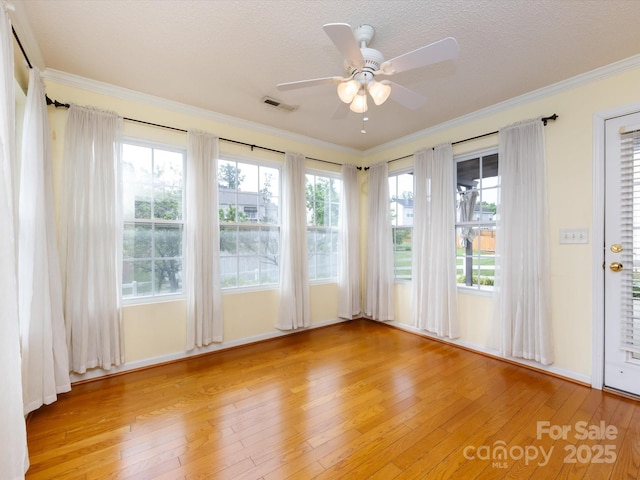 interior space with ceiling fan, ornamental molding, light wood-style floors, and visible vents