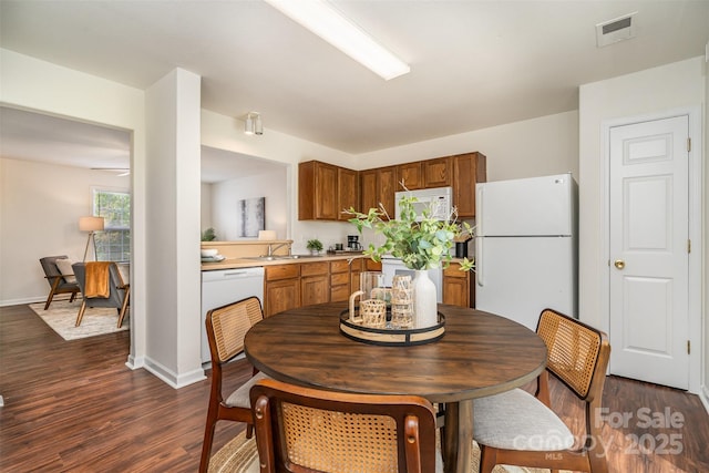 kitchen with white appliances, dark wood-style floors, light countertops, visible vents, and brown cabinets