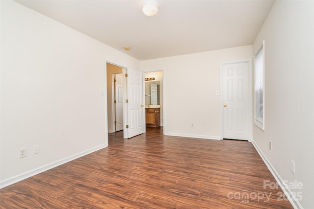 unfurnished bedroom with ensuite bath, dark wood-style flooring, and baseboards