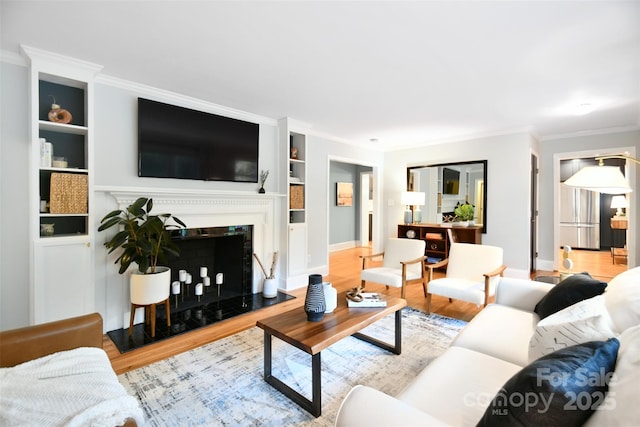 living room featuring ornamental molding, wood finished floors, a premium fireplace, baseboards, and built in shelves