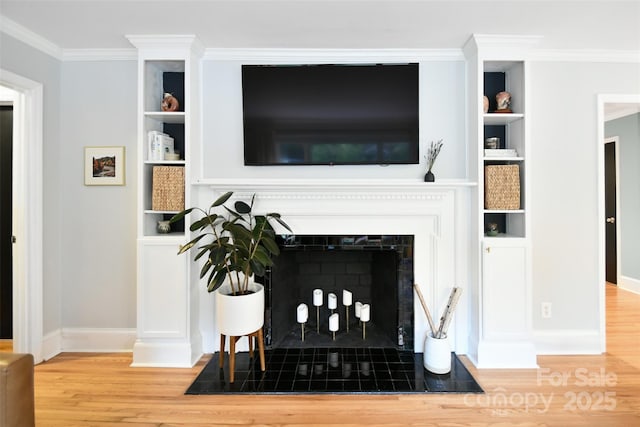 living room featuring built in features, crown molding, wood finished floors, and a tile fireplace