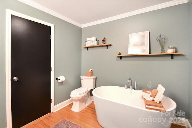 full bathroom with ornamental molding, toilet, wood finished floors, a freestanding bath, and baseboards