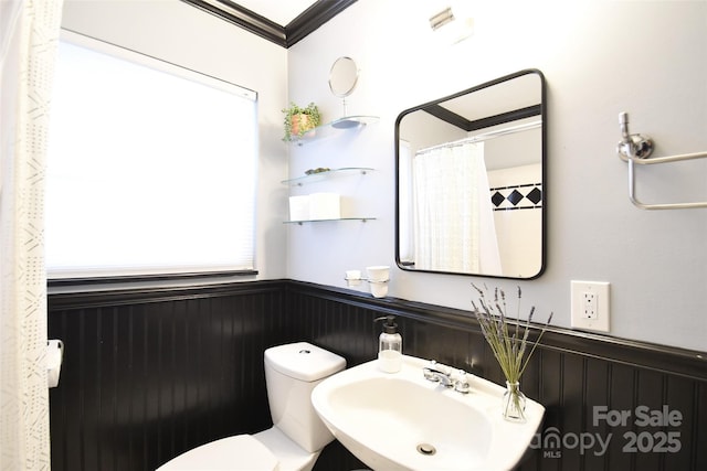 bathroom featuring toilet, crown molding, a sink, and a wainscoted wall