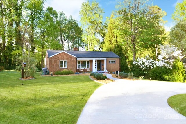 ranch-style home featuring a chimney, concrete driveway, a front lawn, and brick siding