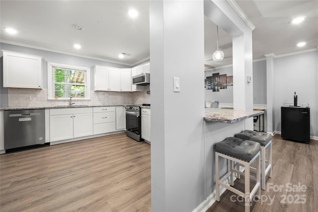 kitchen with ornamental molding, light stone counters, white cabinetry, light wood-style floors, and appliances with stainless steel finishes