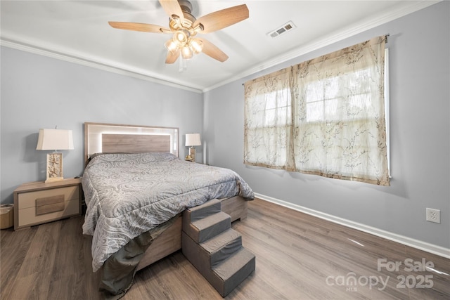 bedroom featuring wood finished floors, visible vents, a ceiling fan, crown molding, and baseboards