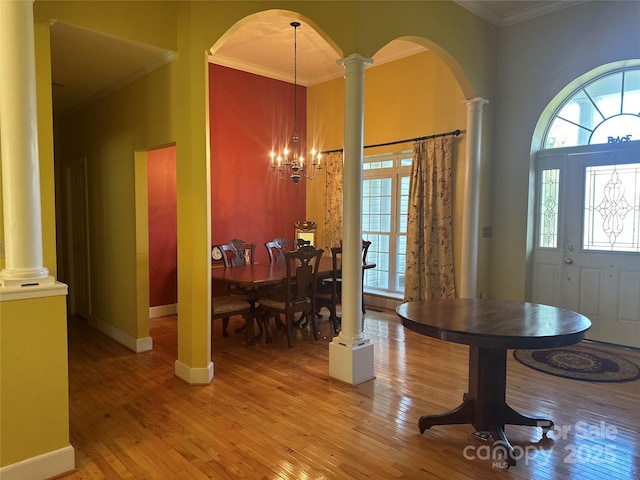foyer featuring a notable chandelier, light wood-style flooring, crown molding, decorative columns, and arched walkways