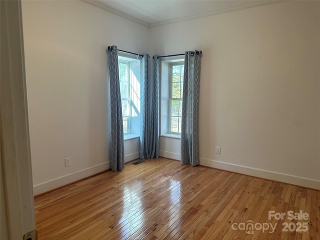 empty room with light wood-style floors, baseboards, ornamental molding, and visible vents