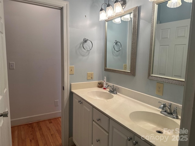 bathroom with wood finished floors, double vanity, a sink, and baseboards
