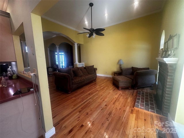living area with light wood-type flooring, a ceiling fan, crown molding, visible vents, and arched walkways