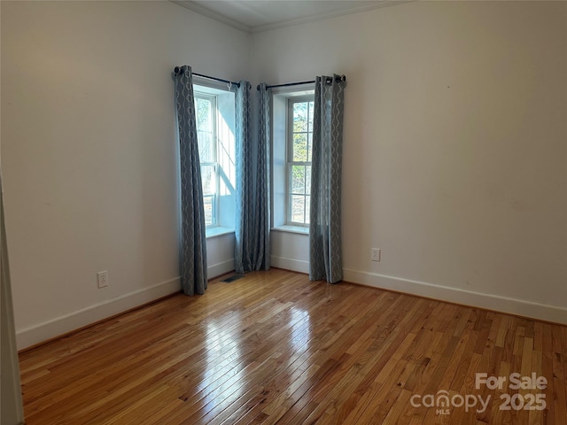 unfurnished room featuring visible vents, baseboards, hardwood / wood-style floors, and ornamental molding