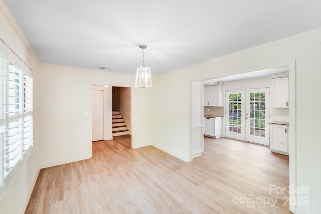 empty room featuring french doors, ornamental molding, light wood-type flooring, and stairs