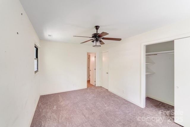 unfurnished bedroom featuring a closet, baseboards, carpet flooring, a walk in closet, and ceiling fan