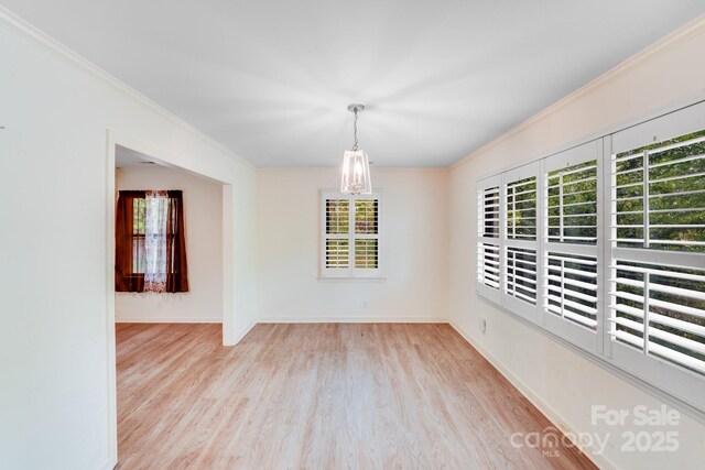 empty room with ornamental molding, baseboards, a notable chandelier, and wood finished floors