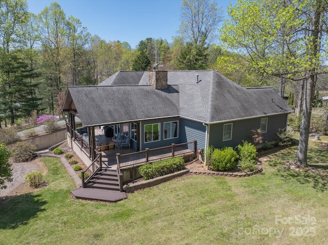 back of property with a yard, a deck, a shingled roof, and a chimney