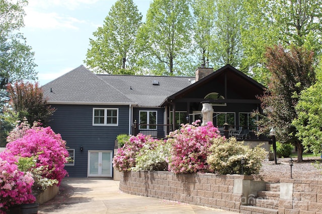 rear view of house with a shingled roof, french doors, and a chimney