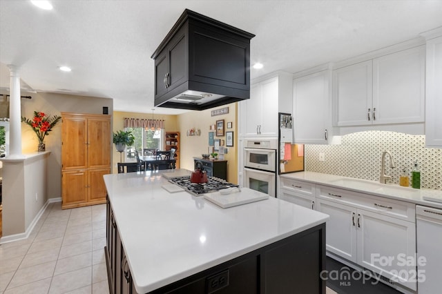 kitchen with decorative columns, a center island, a sink, light countertops, and white appliances