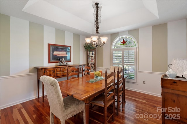 dining area with baseboards, a tray ceiling, a notable chandelier, and wood finished floors