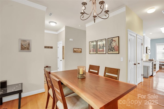 dining room featuring baseboards, ornamental molding, a chandelier, light wood-style floors, and visible vents