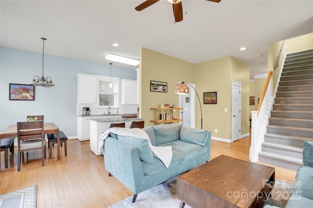 living area featuring recessed lighting, light wood-style flooring, stairs, visible vents, and ceiling fan with notable chandelier