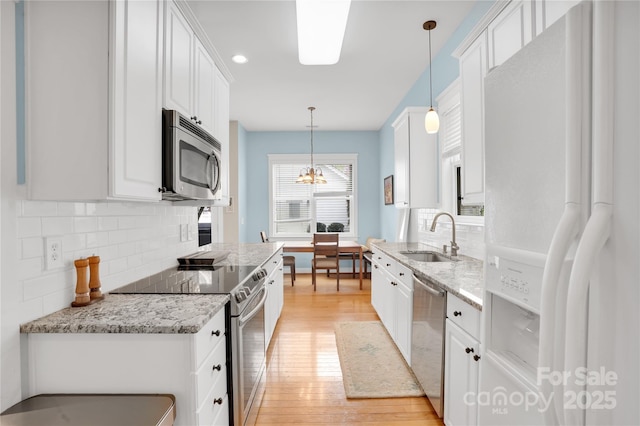 kitchen with light wood-type flooring, white cabinets, appliances with stainless steel finishes, a sink, and backsplash