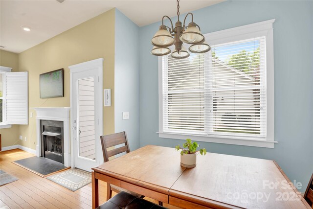 dining space featuring a fireplace, a notable chandelier, baseboards, and hardwood / wood-style floors