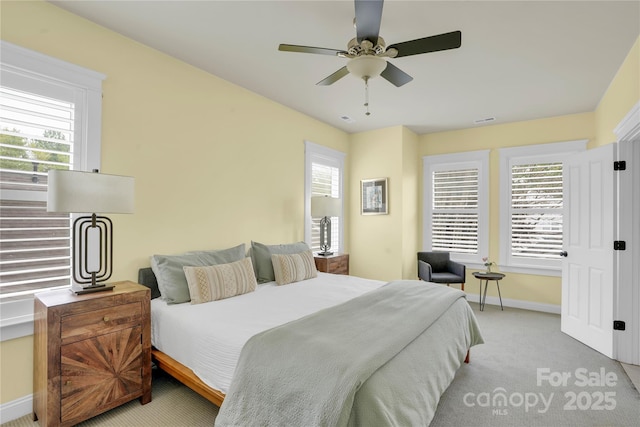 carpeted bedroom featuring visible vents, baseboards, multiple windows, and a ceiling fan
