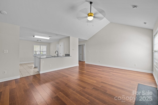 unfurnished living room featuring baseboards, a sink, a ceiling fan, light wood-style flooring, and lofted ceiling