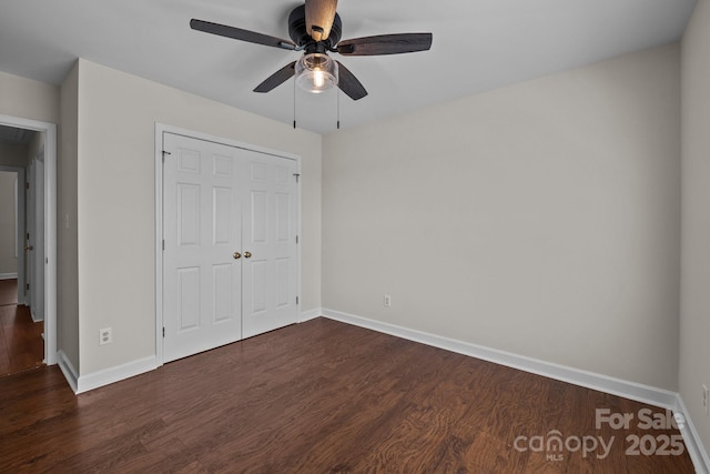unfurnished bedroom with a closet, dark wood-style flooring, baseboards, and a ceiling fan