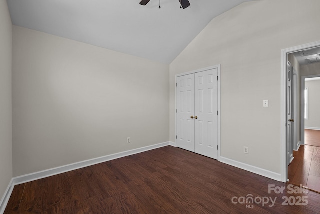 unfurnished bedroom featuring a closet, baseboards, attic access, dark wood-type flooring, and high vaulted ceiling