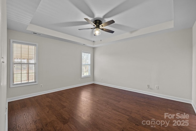 unfurnished room with a tray ceiling, a ceiling fan, visible vents, dark wood-style flooring, and baseboards